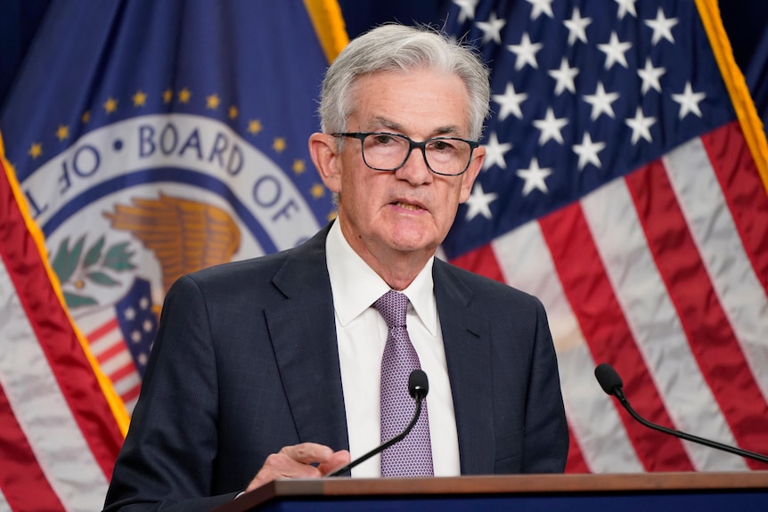 Jerome Powell stands at a podium behind a wall of American flags. 