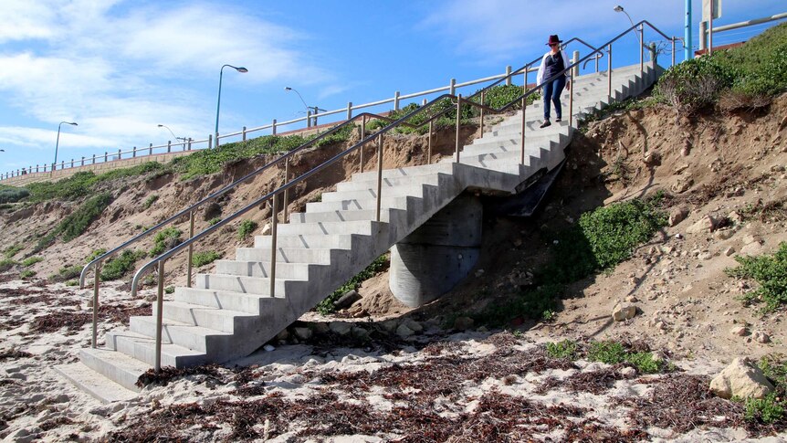 Sand erosion around cement steps leading down to a beach.