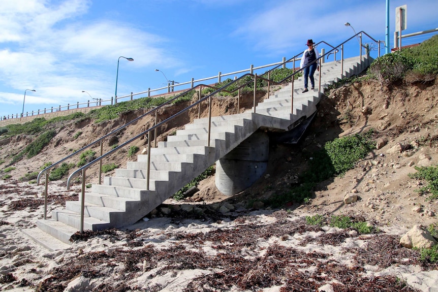 Sand erosion around cement steps leading down to a beach.
