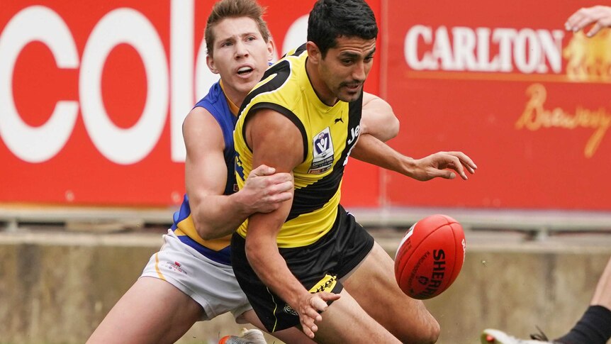 Marlion Pickett is tackled by a Williamstown seagulls player and looks at the ball as he falls to his knees