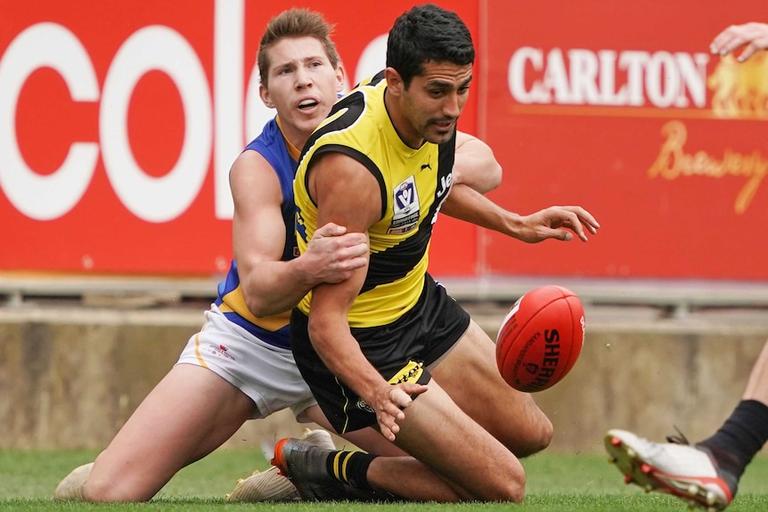 Marlion Pickett is tackled by a Williamstown seagulls player and looks at the ball as he falls to his knees