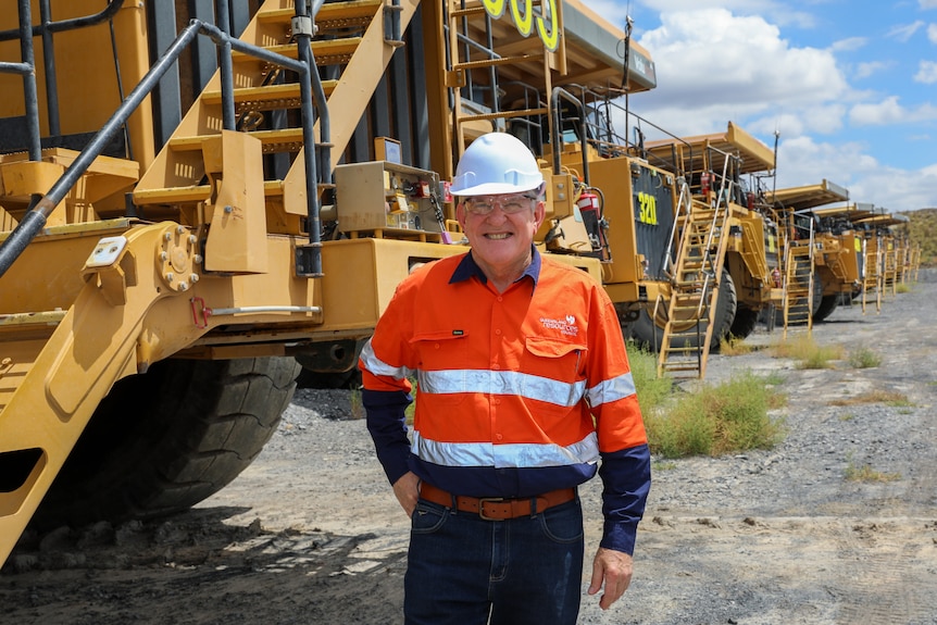 A man in high vis smiles. There is heavy machinery behind him.