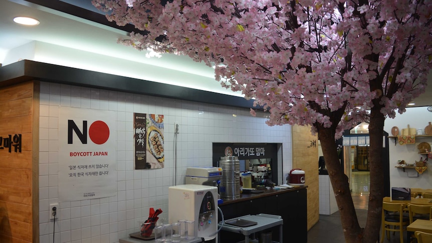 A fake cherry blossom tree stands in a Japanese franchise restaurant in Gwangju, South Korea, next to a "Boycott Japan" poster