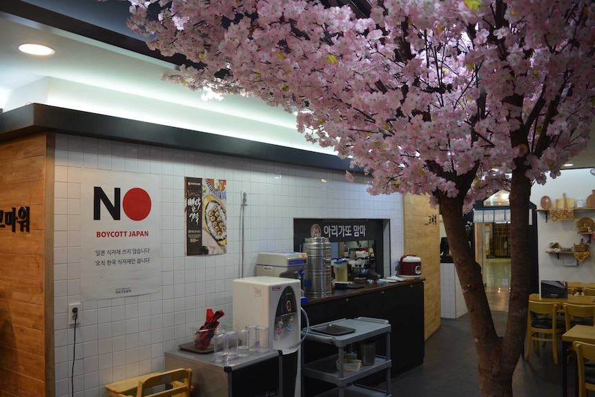 A fake cherry blossom tree stands in a Japanese franchise restaurant in Gwangju, South Korea, next to a "Boycott Japan" poster