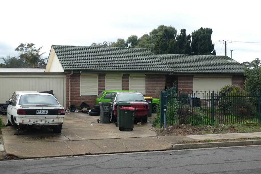 A house with damaged cars and bins in front