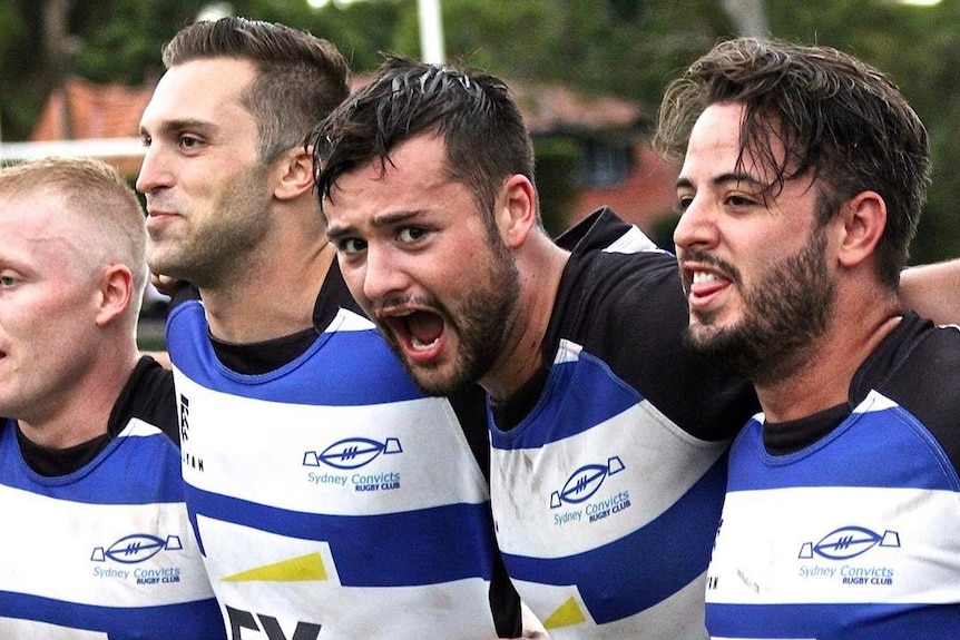 Four men wearing jerseys stand shoulder to shoulder while singing.