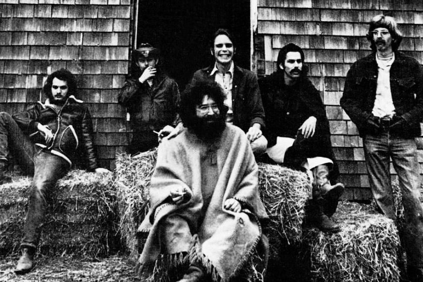 Black and white image of six men lounging on haybales