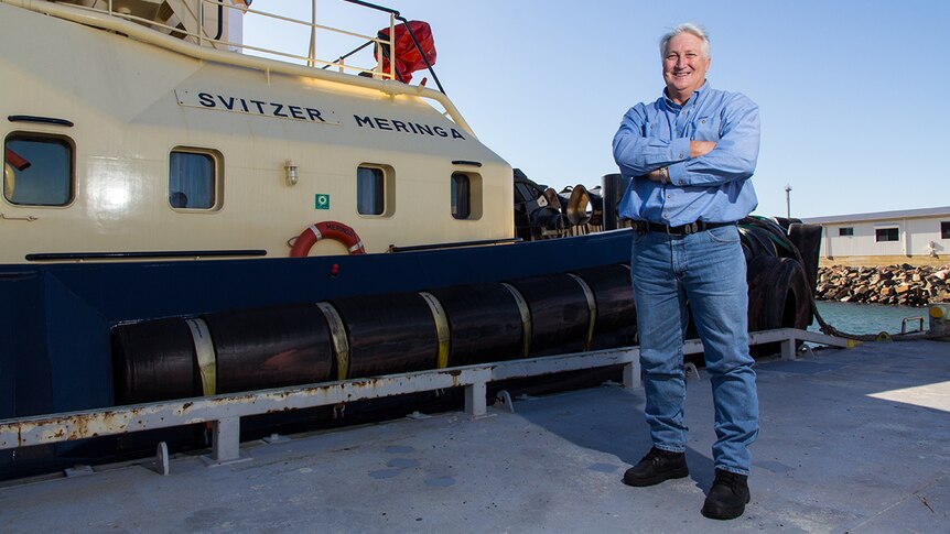 Aaron Henshaw stands on the dock next to a moored tugboat.