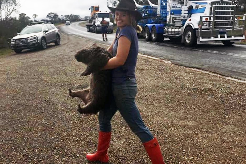 A woman in bright red boots carries a wet wombat.
