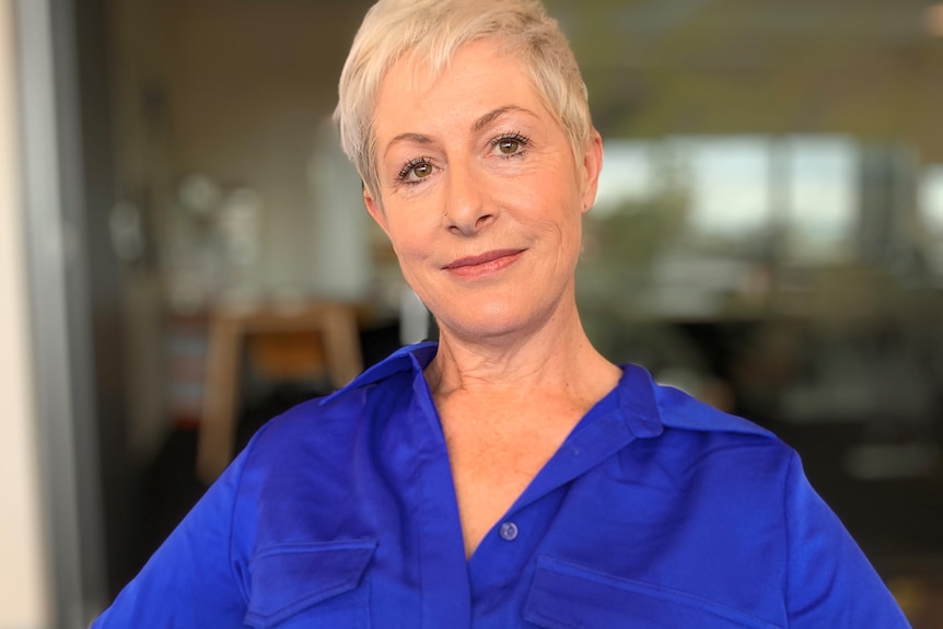 A woman in a blue blouse is looks into camera.