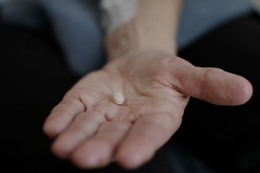 A woman holds a pill on her hand