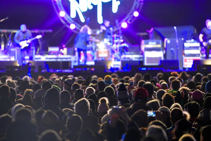 a cluster of people standing in front of a stage with a band on it