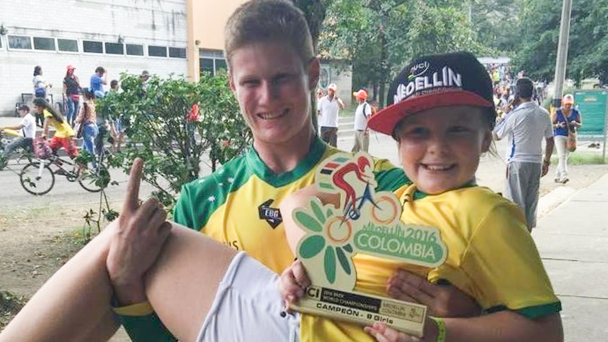 Portia Eden, holding her world championship trophy, is held up in the air by her coach, Ronan Weber.