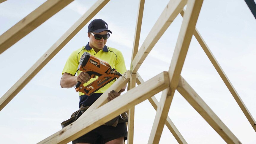 A photo of a carpenter holding a drill on a roof at construction site