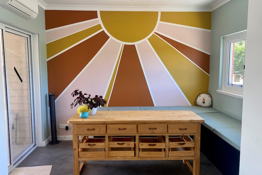 A small kitchen with a mural of a sun on the wall. 