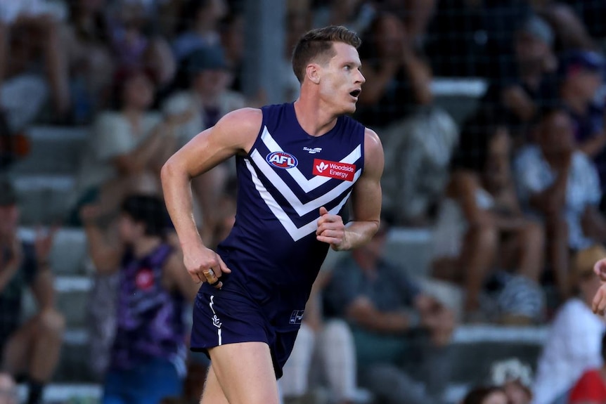 A man in a purple football top running across the field. 