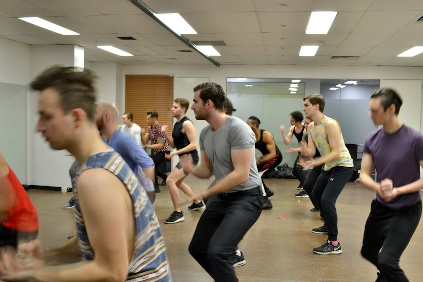 A group of men dance in a studio space.