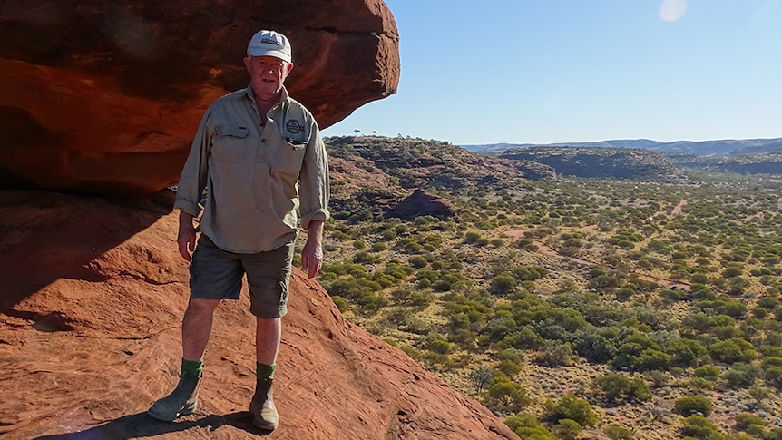 Doug Lang stands in a rugged landscape next to a large rock.