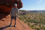 Doug Lang stands in a rugged landscape next to a large rock.