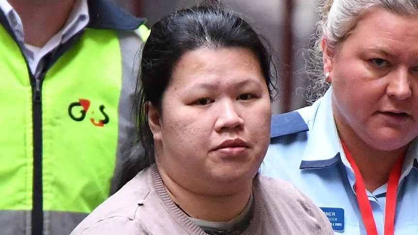 Amy Tran is dressed in a light jumper as she is led by prison officers from a van into a court building.