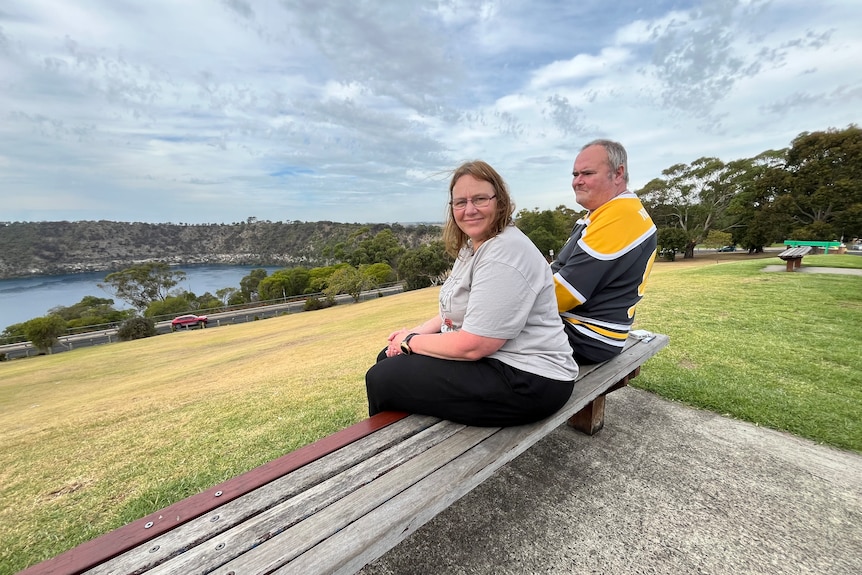 A woman and a man sit on a park bench overlooking a lake.
