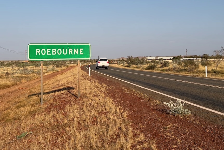 A white four-wheel drive passes a street sign that reads 'Roebourne'.