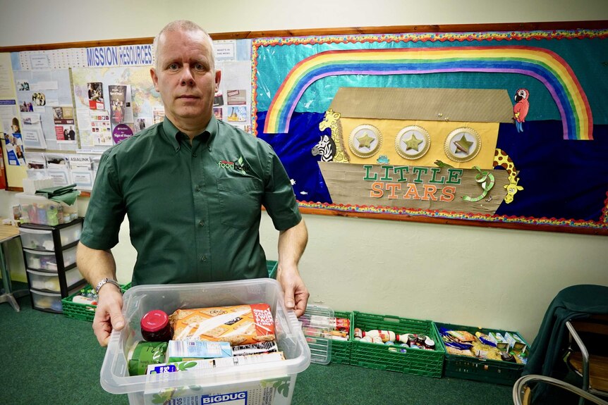 A man holds a container of non-perishable food in a food bank.
