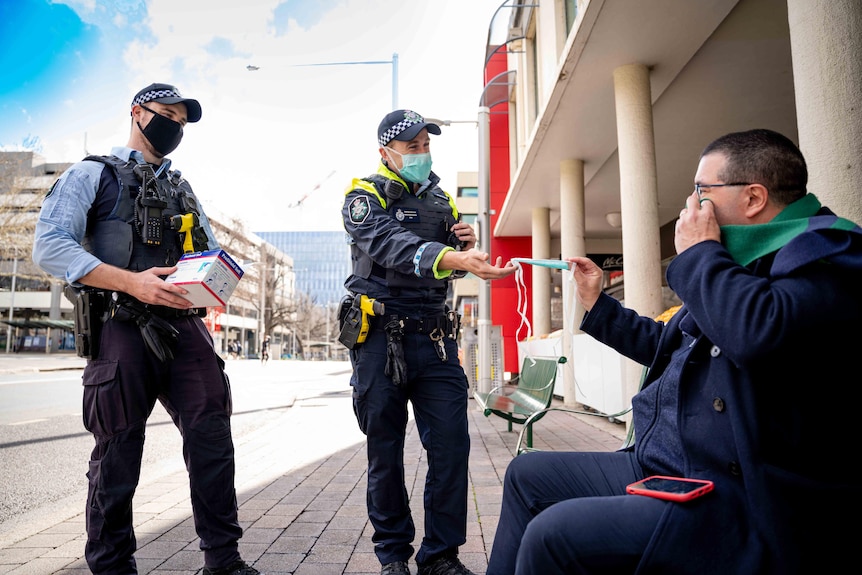 Two policemen walk through Canberra and give a man a mask