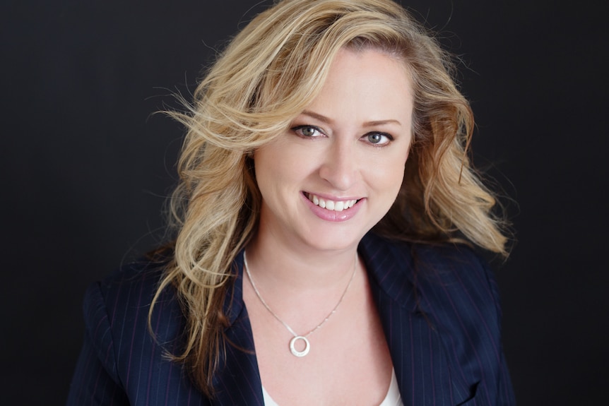 woman with blonde hair stands smiling at the camera