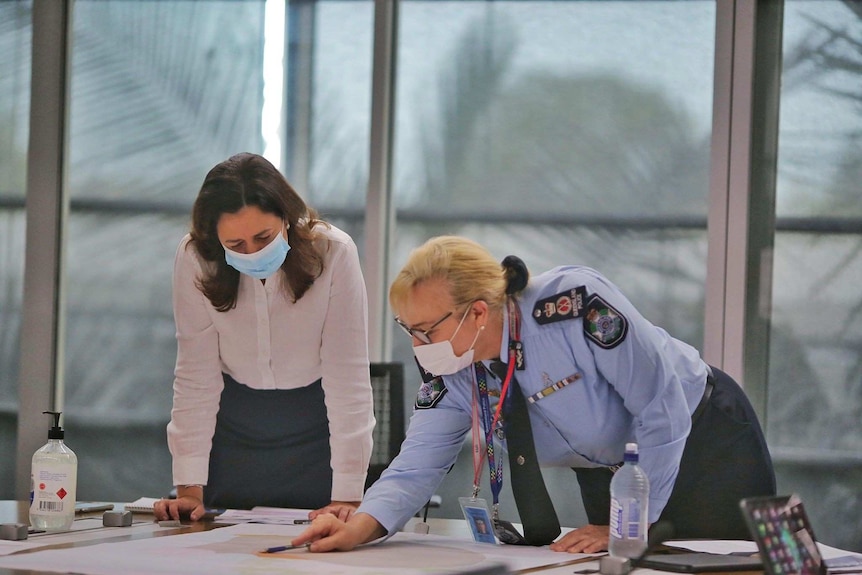 Two women in face masks look at a map on a table.