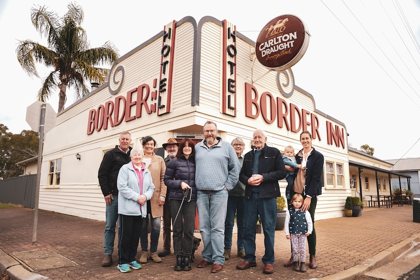 A group of men and women stand on a street corner in front of a large building with the words 'Border Inn'.