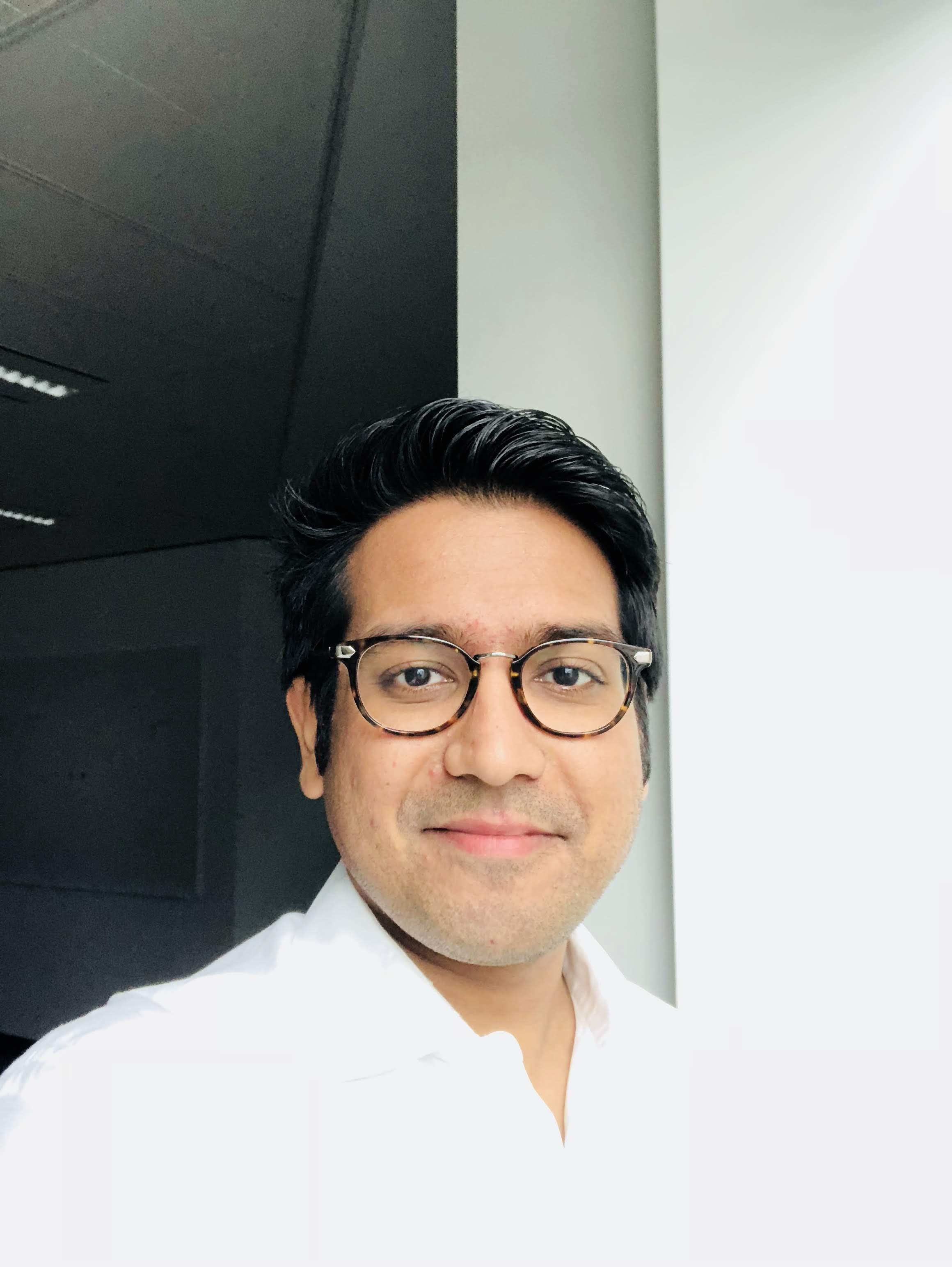 Man with dark hair and wearing glasses smiles at the camera.