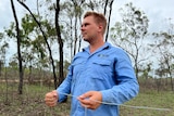 Roman Dubinchak in light blue workshirt and work pants holds two rods he uses for water divining