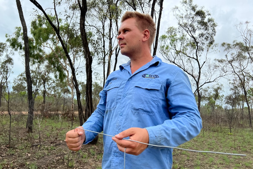 Roman Dubinchak in light blue workshirt and work pants holds two rods he uses for water divining