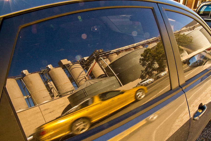 Car window reflection showing ute driving past grain silos in a regional town to depict a tree change.
