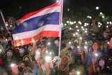 People sitting in rain coats waving lights from smartphones and a Thai flag at night