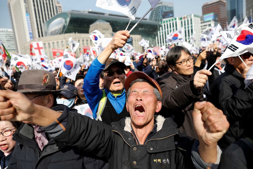 People waving South Korean flags and a man screaming with his fists clenched as the focus of the photo