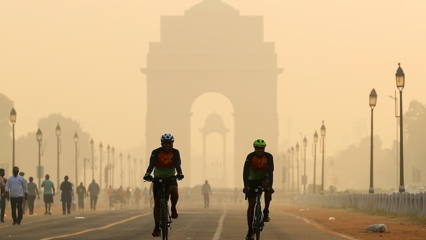 Men ride their bicycles in front of the India Gate shrouded in smog.