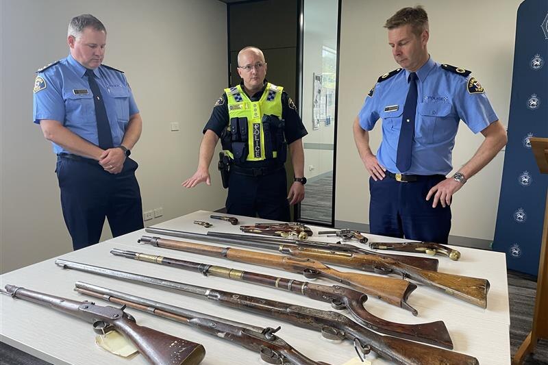 Antique firearms on display, with Tasmania Police officers standing by.
