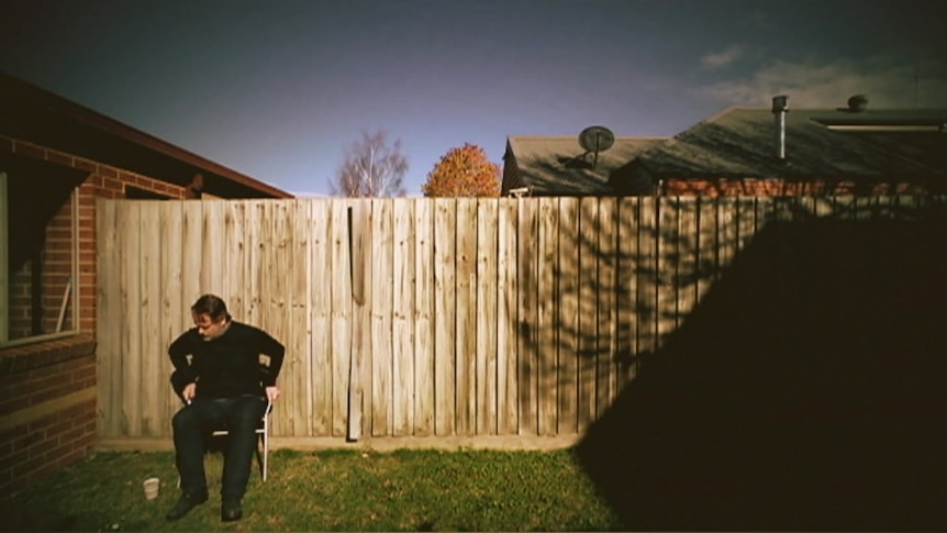 Martin Rollins sitting in chair near the side fence of his backyard