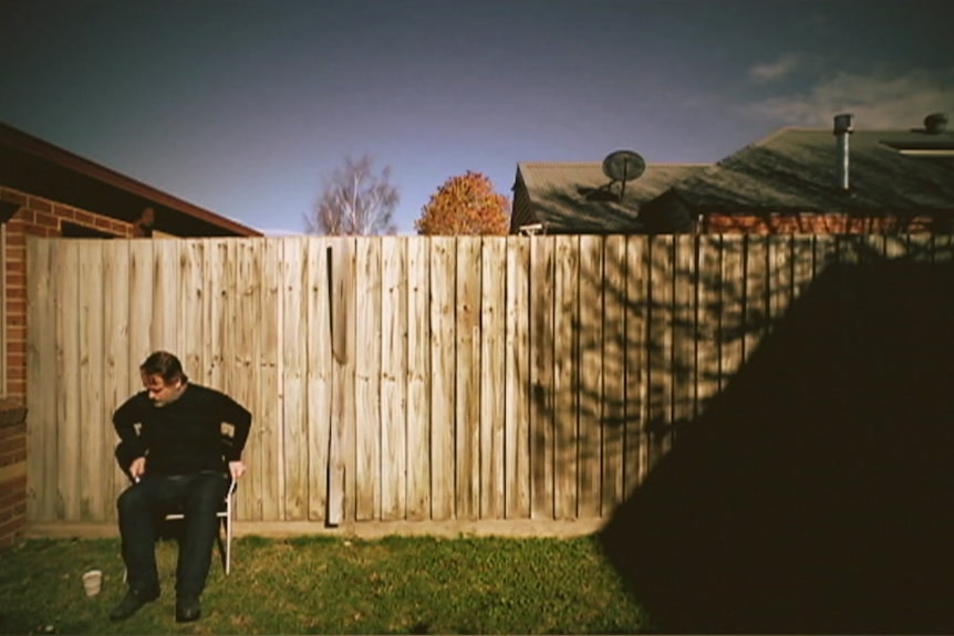 Martin Rollins sitting in chair near the side fence of his backyard