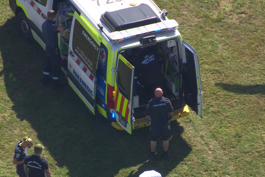 An ambulance surrounded by paramedics in a field.