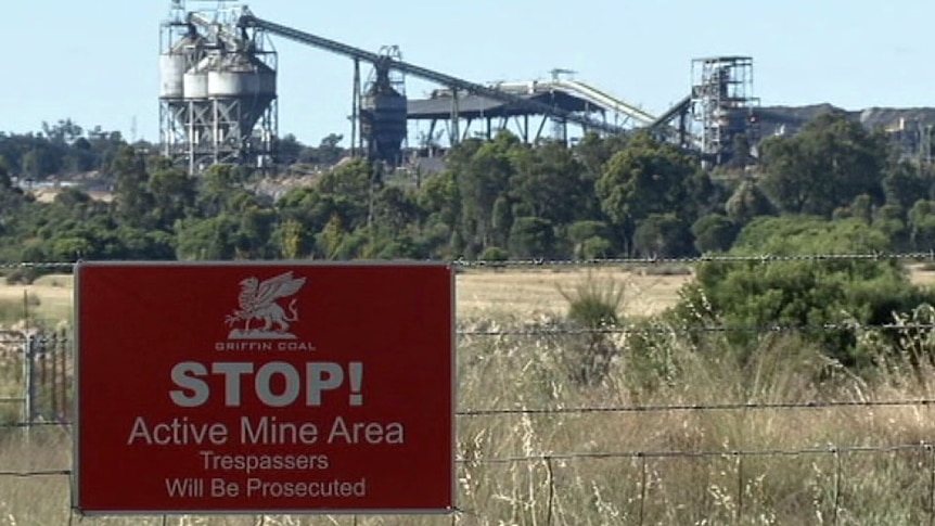 A distant mine behind a wire fence with a sign reading 'Stop! Active mine area. Trespassers will be prosecuted'