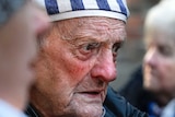 A profile of an ageing male survivor wearing a stripe cap and top.
