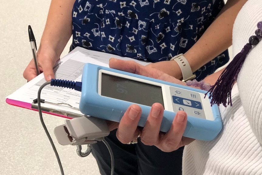 A woman holds a blue heart rate monitor while a nurse stands nearby 