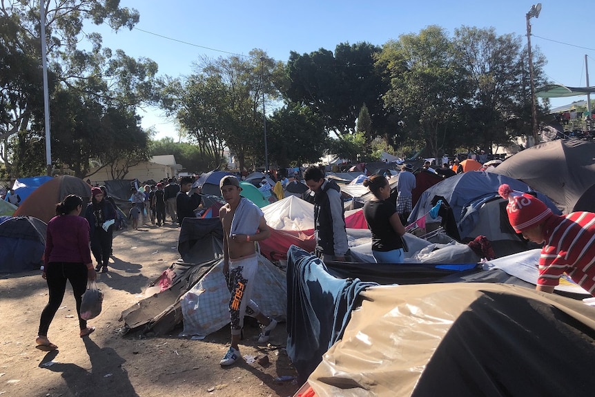 People of all ages move among tents erected in a large camp