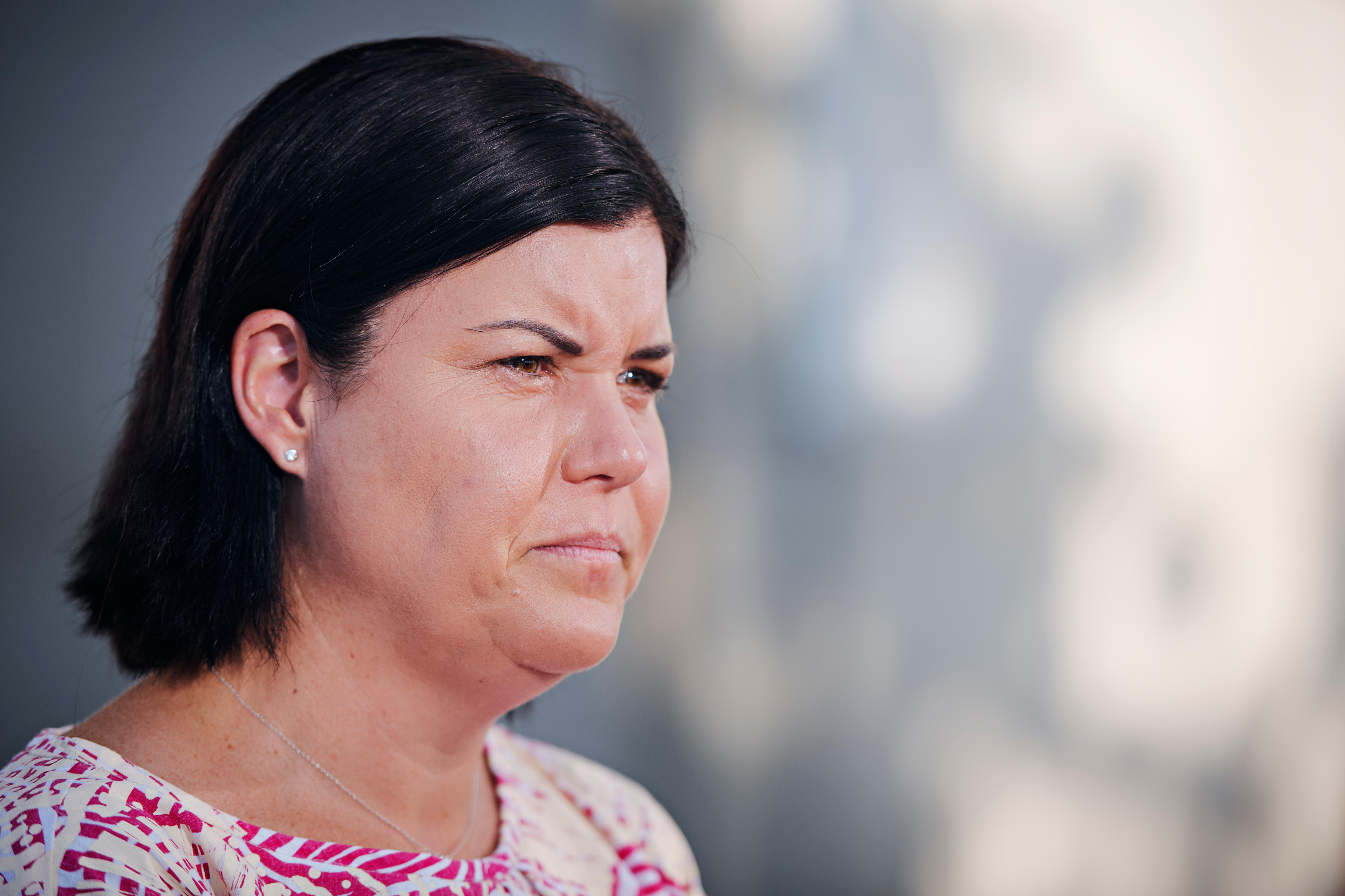 A woman with dark short hair and a pink and orange patterned dress squints.