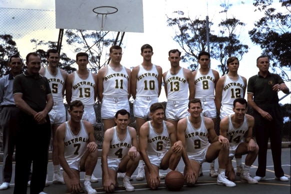 Twelve men in Australian basketball jerseys pose for a photo on an outdoor court.