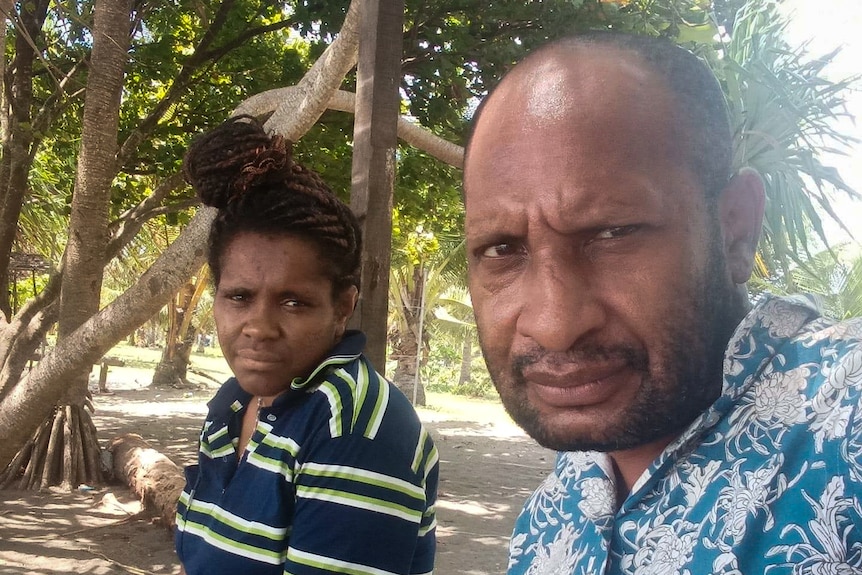 A man wearing a bright blue shirt with floral pattern sits next to a woman in striped polo shirt