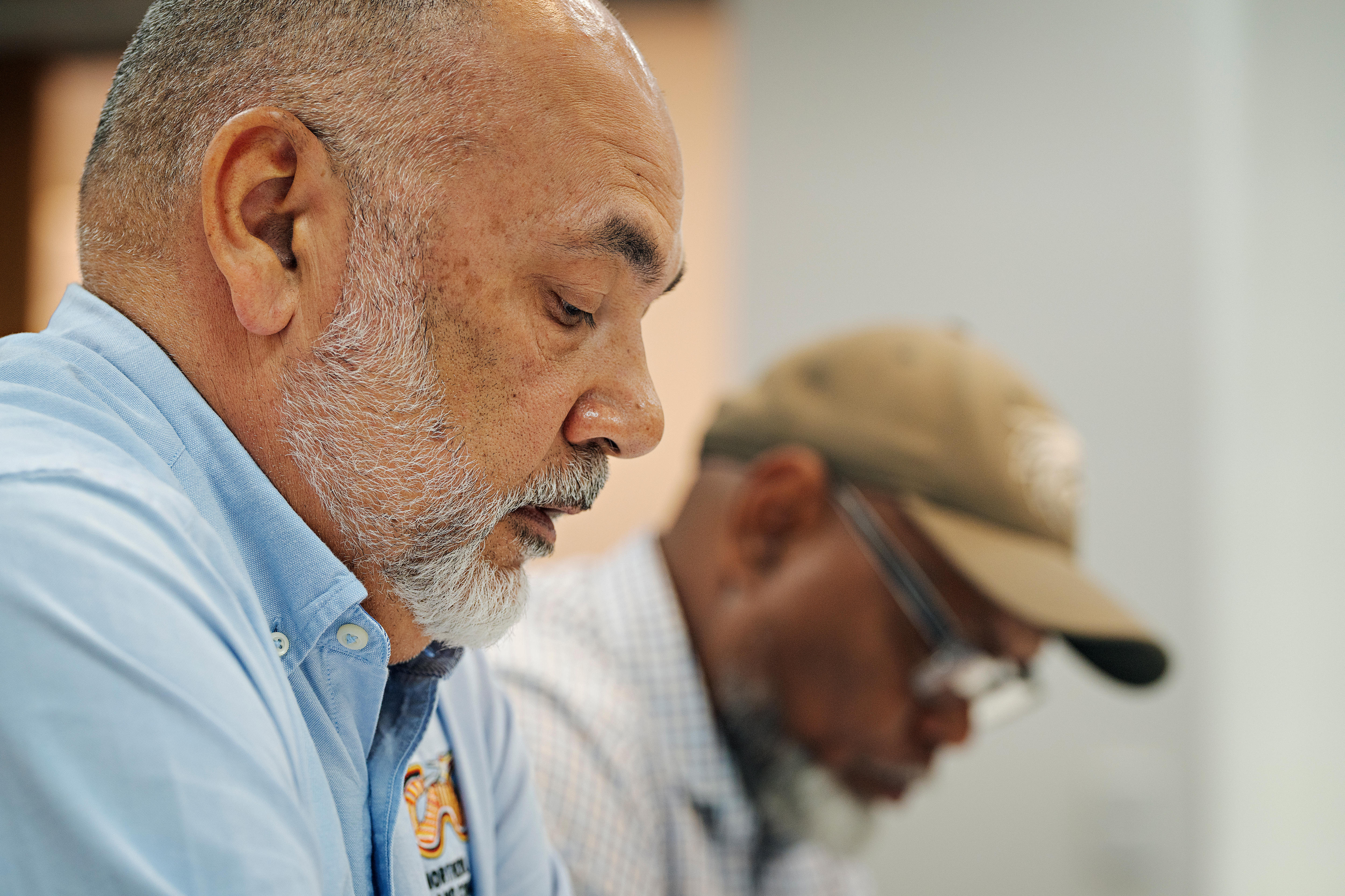 A man in a blue collared shirt with a white beard is looking down